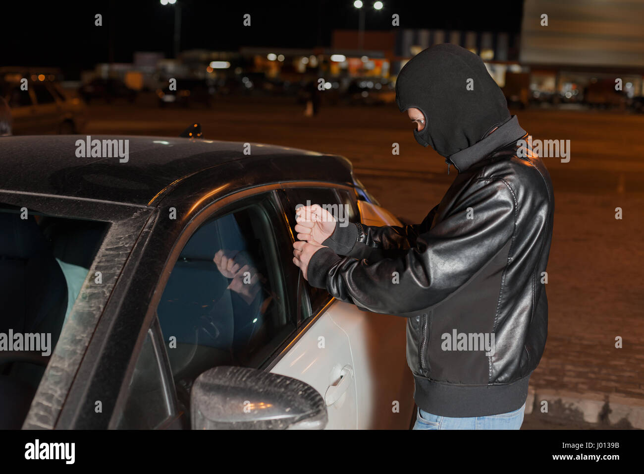 Male carjacker with balaclava on his head trying to open car door with ruler. Thief unlock vehicle. Auto transport insurance marketing Stock Photo