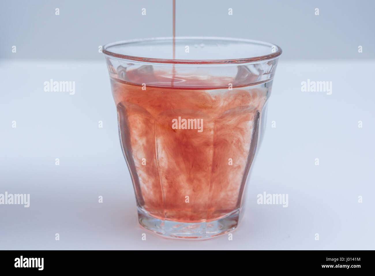 fruit juice extract poured into glass of water on white background