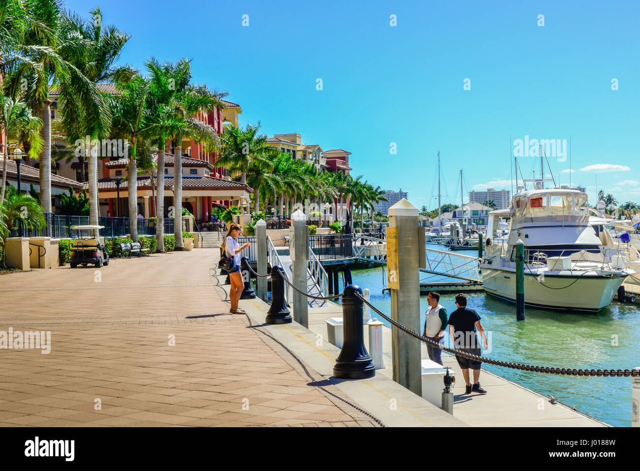 The esplanade waterfront lined with upmarket buildings and palm trees with people and boats on Smokehouse Bay on Marco Island, FL Stock Photo