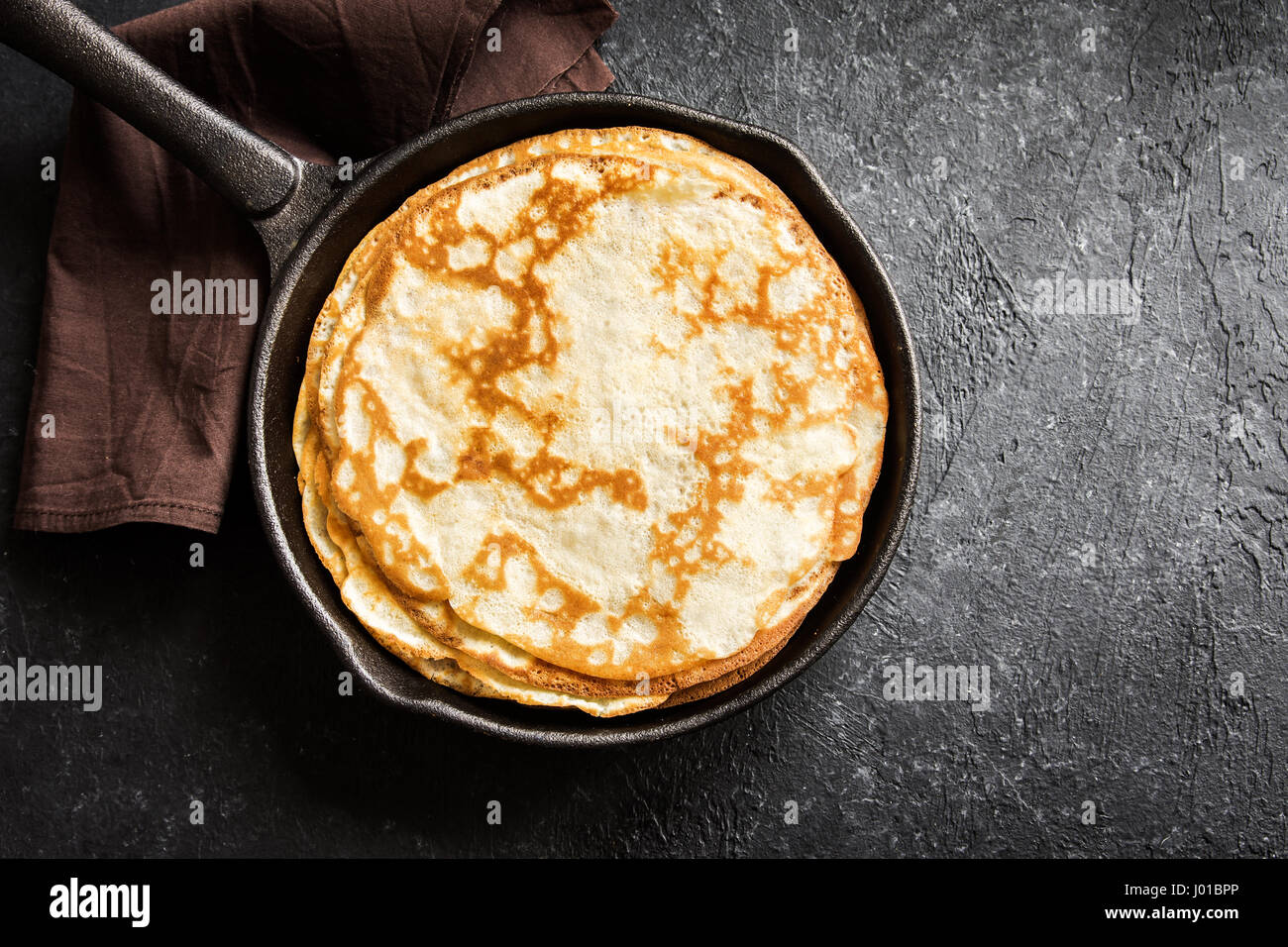 Homemade crepes in cast iron pan over rustic black background with copy