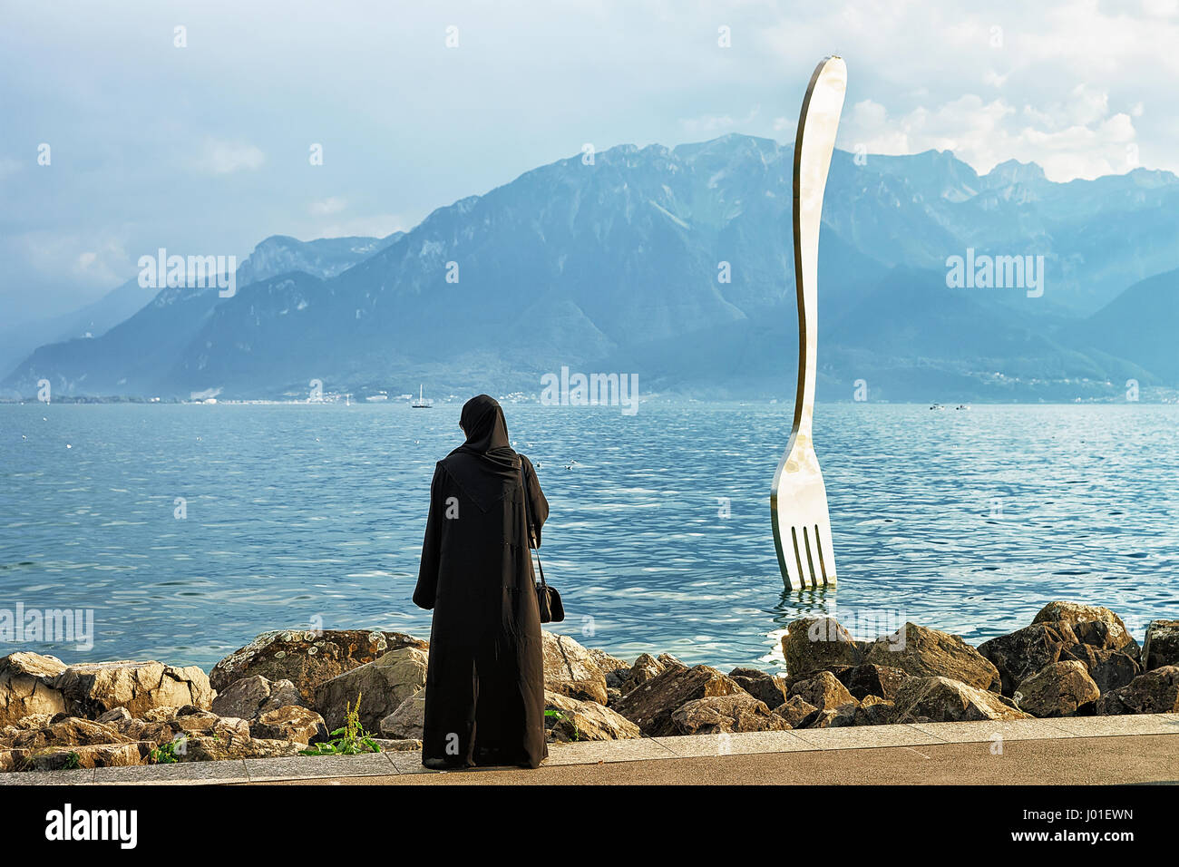 Vevey, Switzerland - August 27, 2016: Muslim woman in black burqa in Fork sculpture at Geneva Lake in Vevey, Vaud canton, Switzerland. Alps mountains  Stock Photo