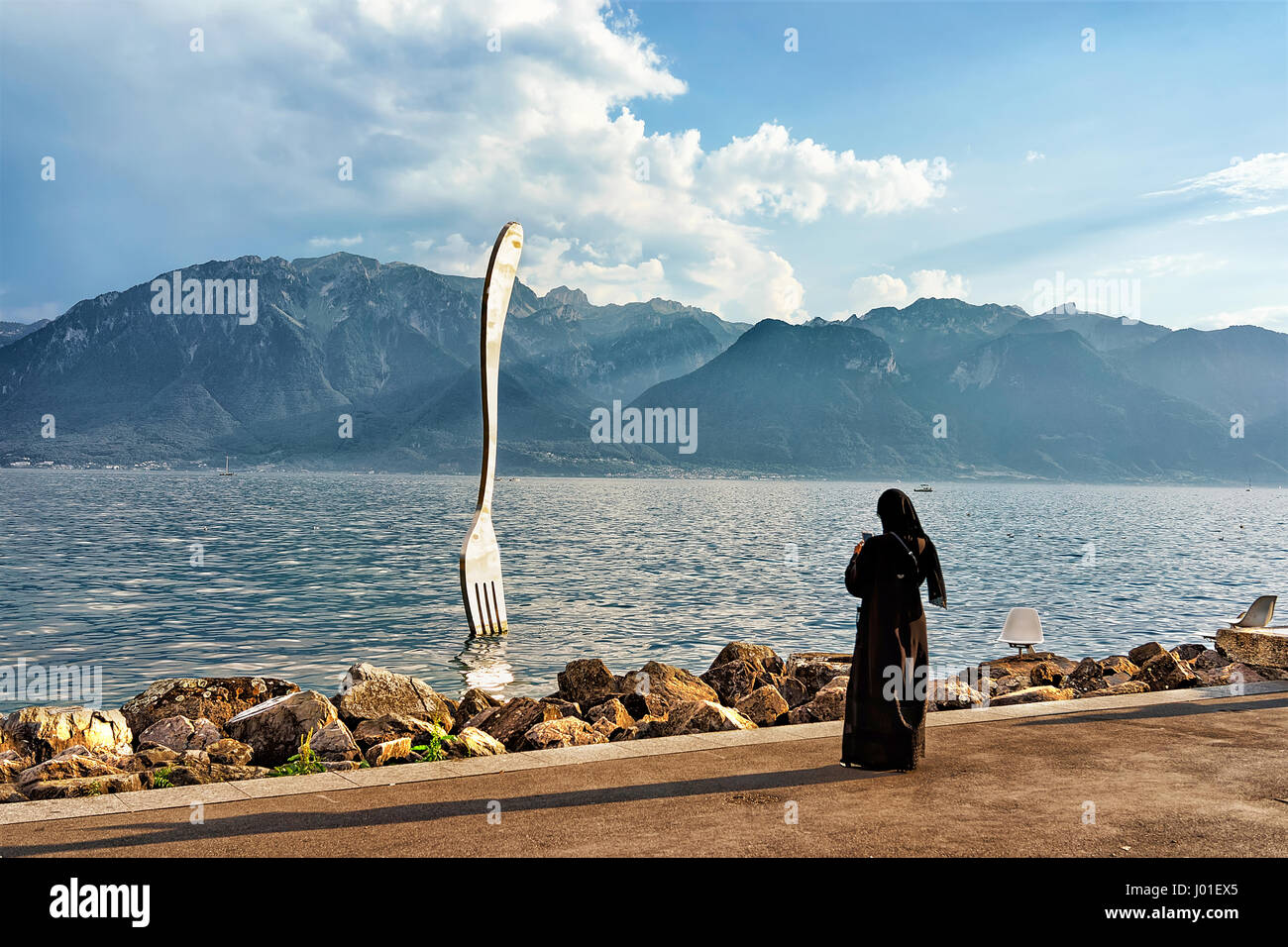 Vevey, Switzerland - August 27, 2016: Muslim woman in black burqa at Fork sculpture at Geneva Lake of Vevey Riviera, Vaud canton, Switzerland. Alps mo Stock Photo