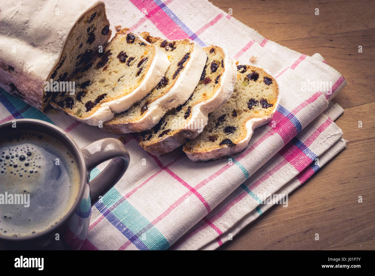 Stollen, traditional German Christmas yeast cake with raisins served with a cup of coffee, decorated with tablecloth on wooden table Stock Photo