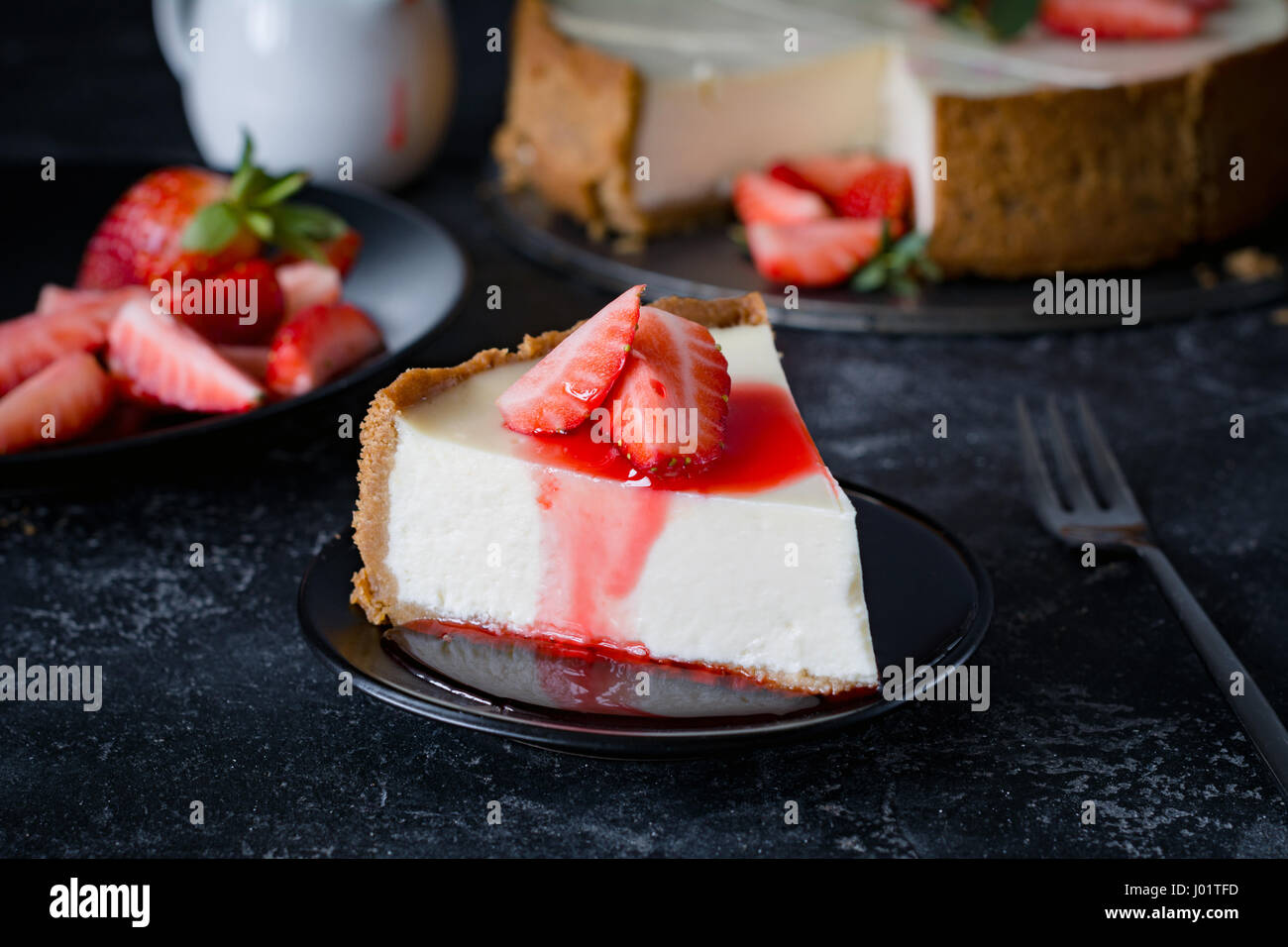 Cheesecake with fresh strawberries and strawberry syrup on black plate