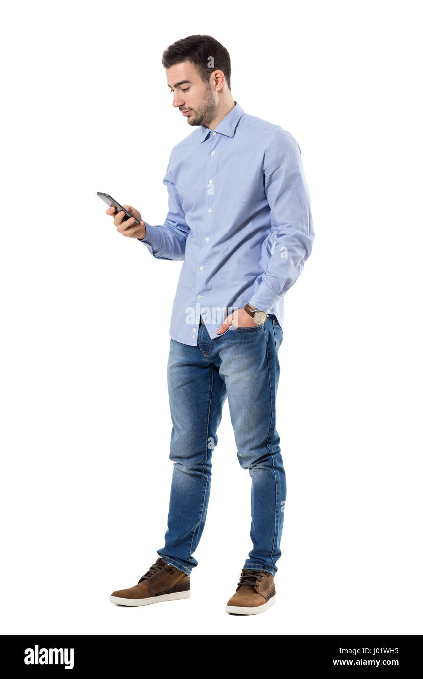 Side view of young smart casual business man reading message on cell phone. Full body length portrait isolated over white background. Stock Photo