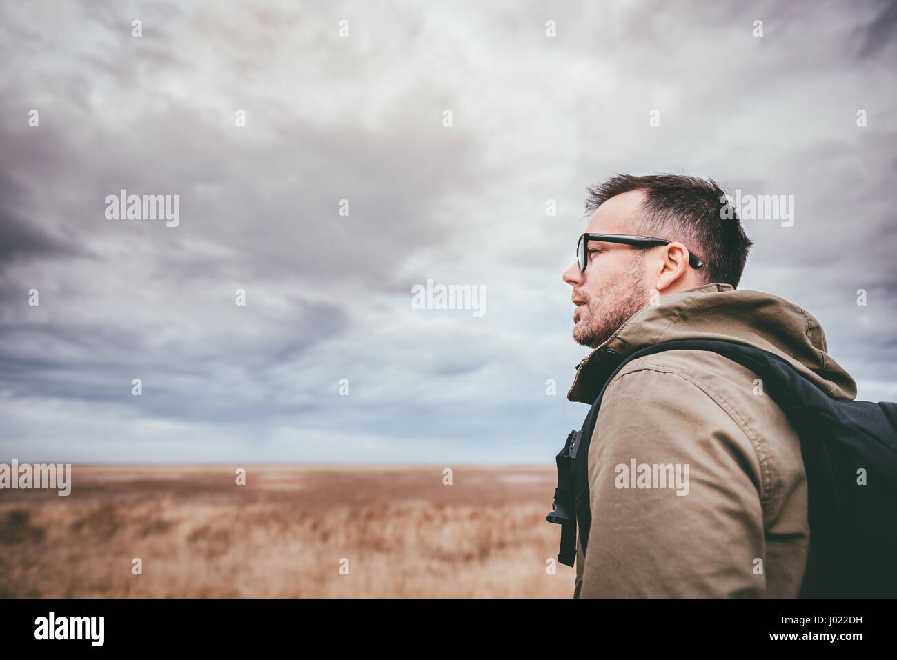 Hiker standing in grassland and looking at distance Stock Photo