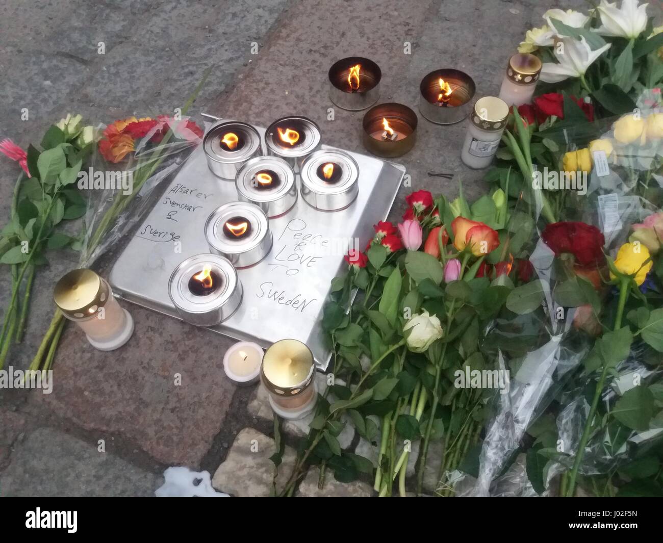 Placard reading Peace and love to Sweden, laid on the ground next to the flower bouquets  laid on the street where Swedish bereave for the lost lives of their compatriots. Stock Photo