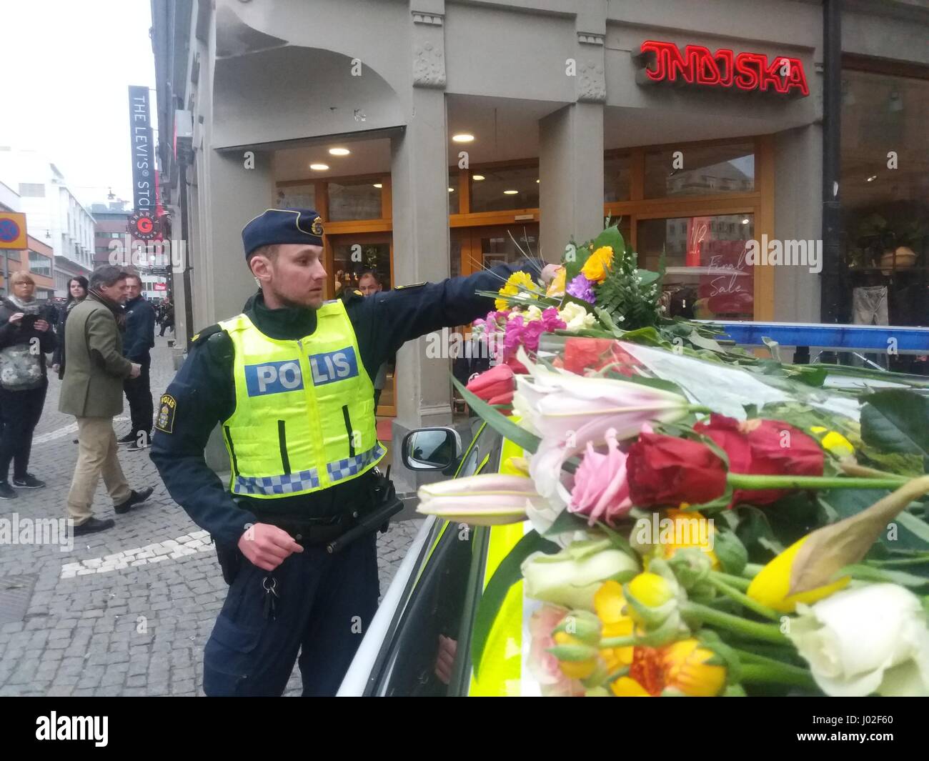 Swedish Polis police officer deposits a flower bouquet on the parked police car roof, given to him by a citizen, in sympathy to the victiims of the terrorist truck attack in the center of Stockholm's Ahlens mall, now being cordoned off due to police investigations in the crime scenes. Stock Photo