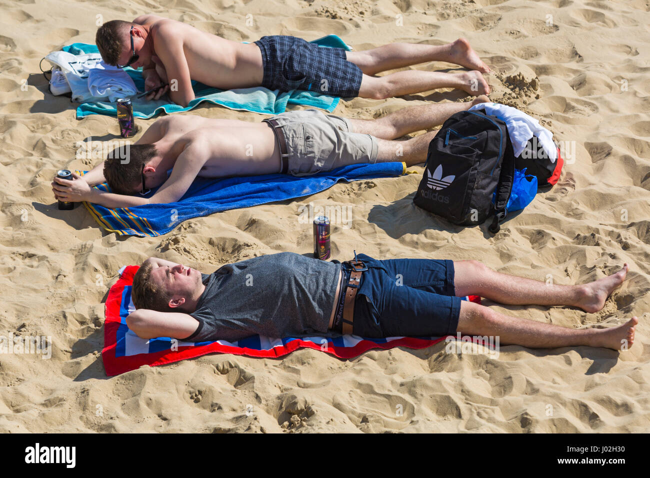 Bournemouth, Dorset, UK. 9th Apr, 2017. UK weather: lovely warm sunny day as visitors head to the seaside to make the most of the sunshine at Bournemouth beaches. Mid day and the beaches are very busy! Three young men sunbathing on the beach Credit: Carolyn Jenkins/Alamy Live News Stock Photo