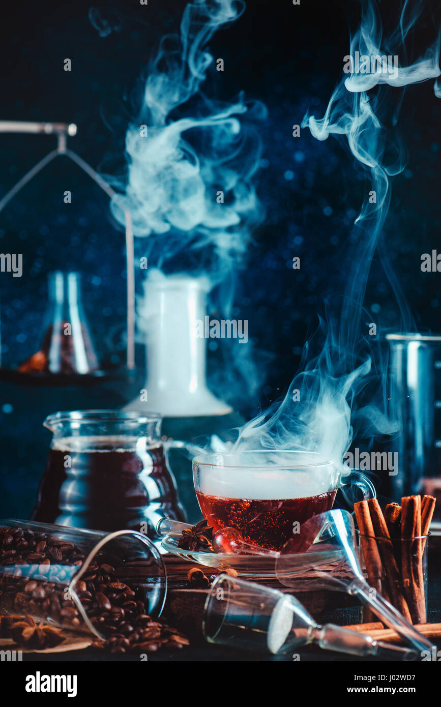 Dark food photo with steaming cup of coffee, cinnamon, laboratory funnel, beakers and test tubes Stock Photo