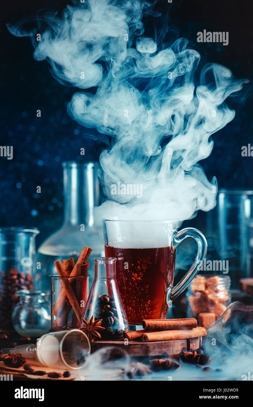 Dark food photo with steaming cup of coffee, spices, anise, and cinnamon, in laboratory setting with funnel, beakers and test tubes Stock Photo