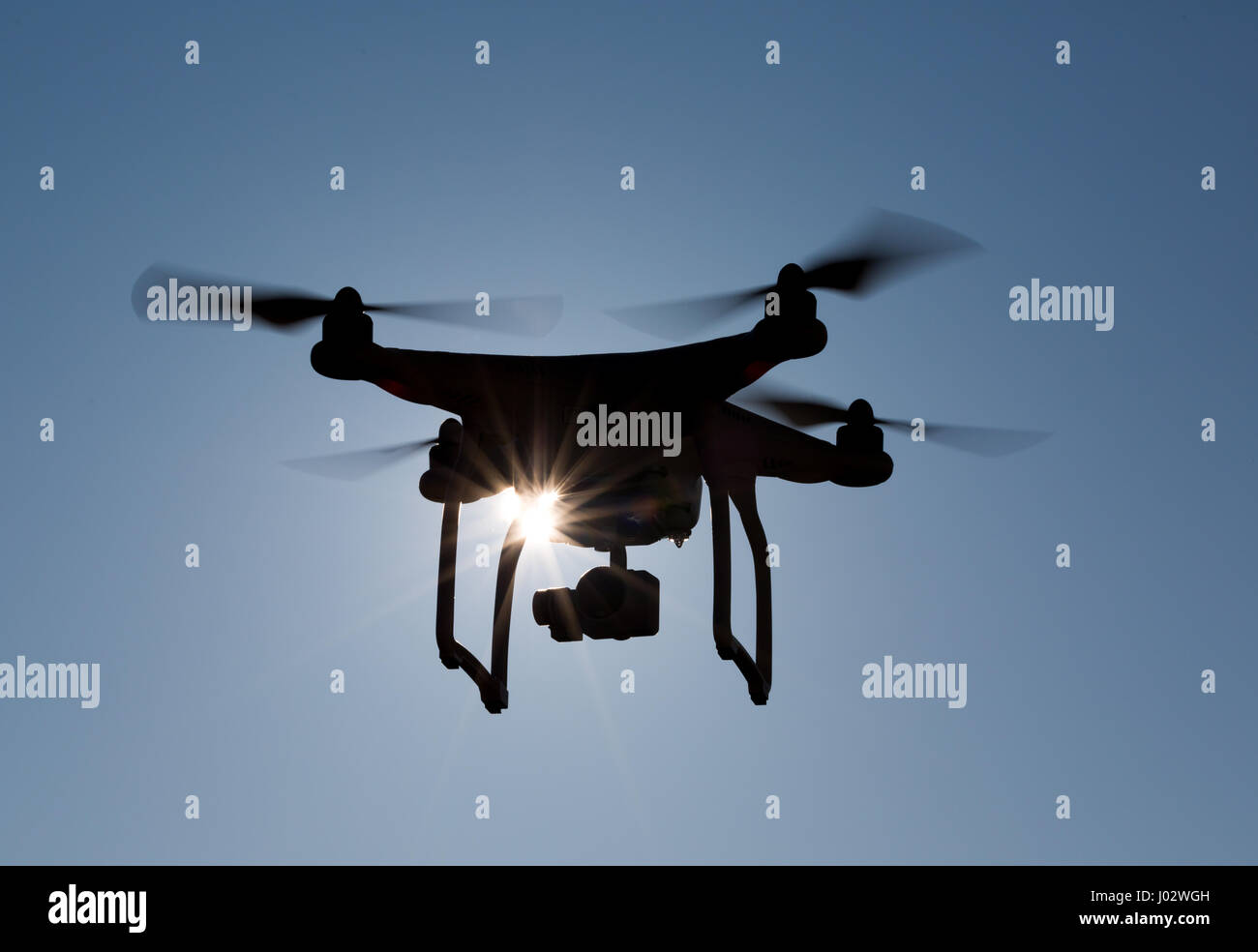 Quadcopter drone flying in front of the sun with backlight, closeup Stock Photo