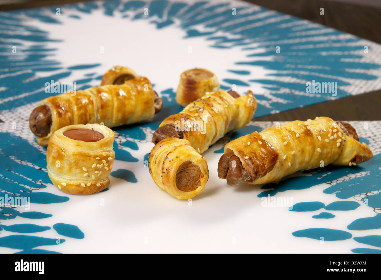 Baked puff pastry hot dog pockets (Vienna sausage hotdog / frankfurter mini pies) on white and light blue placemats - Close up, bokeh background Stock Photo