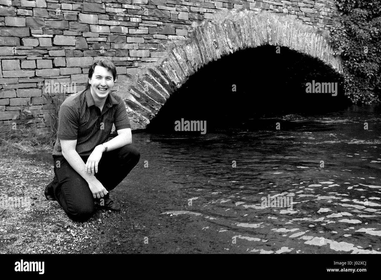 A young man by a bridge and river (black and white) Stock Photo