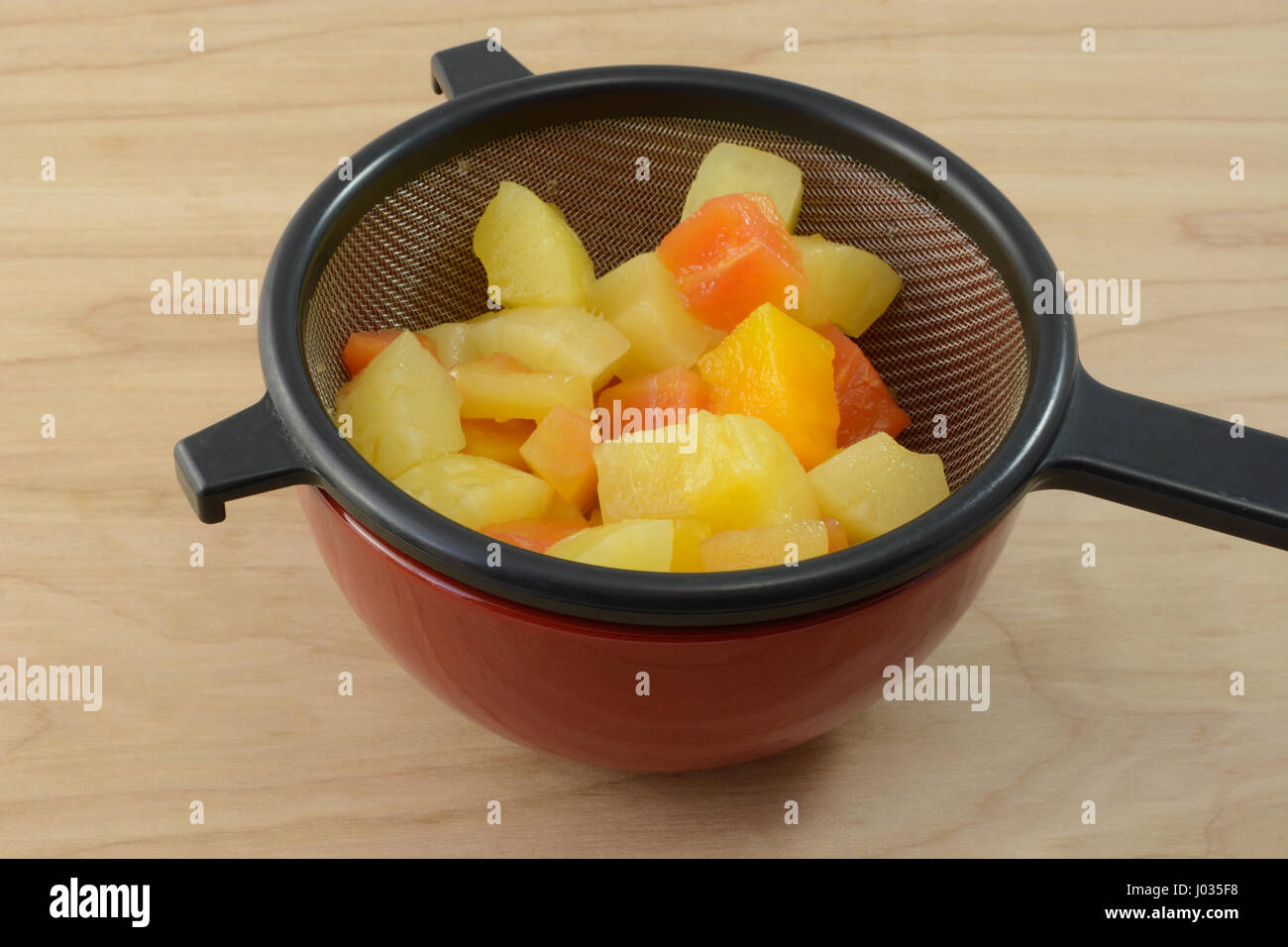 Canned tropical fruit mix of pineapple and papaya draining in strainer