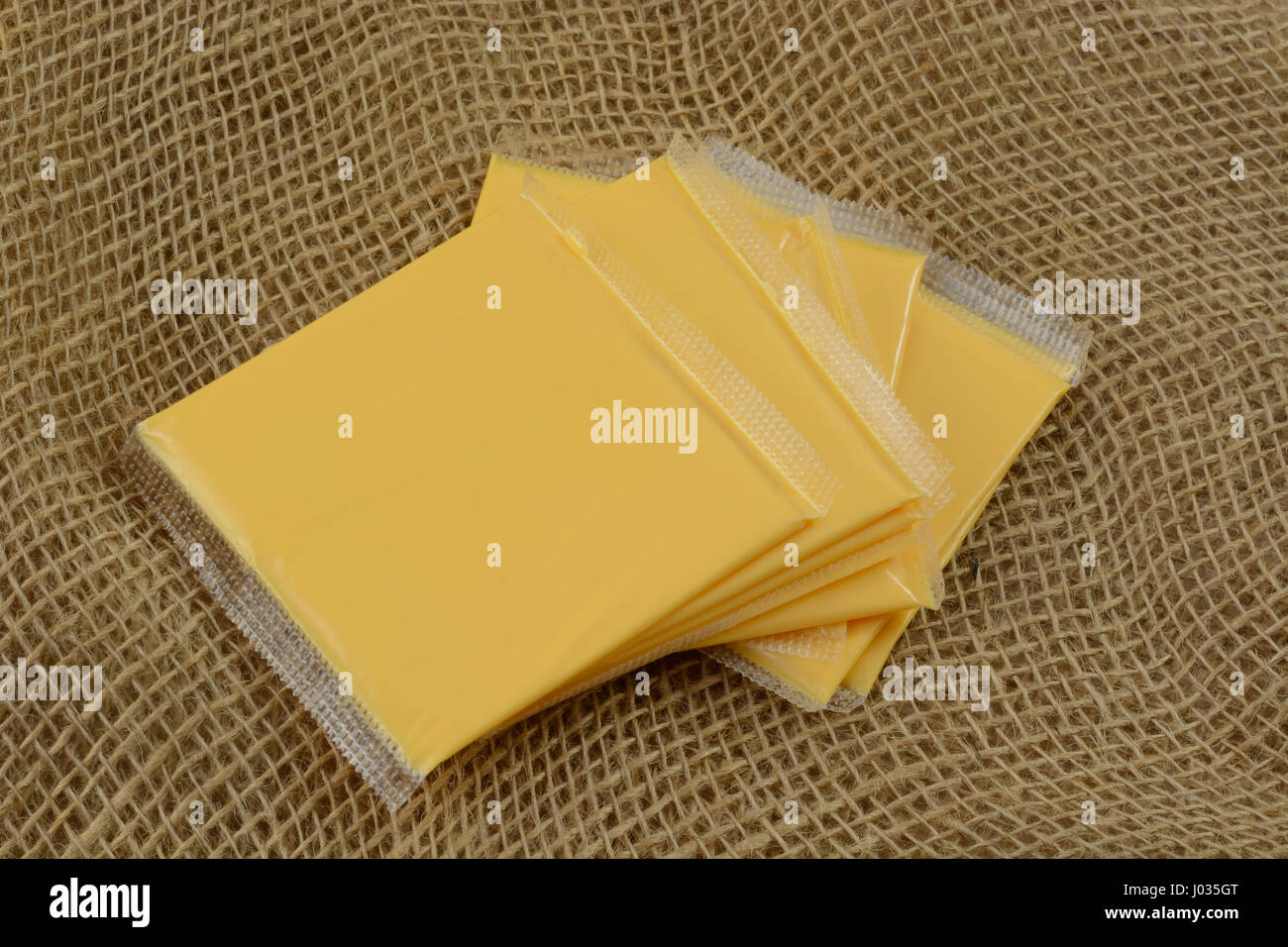 Stack of American cheese slices in plastic packaging on burlap Stock Photo