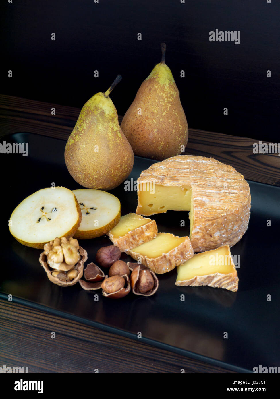 Soft washed-rind cheese, walnut, hazelnuts and pears on the black plate Stock Photo