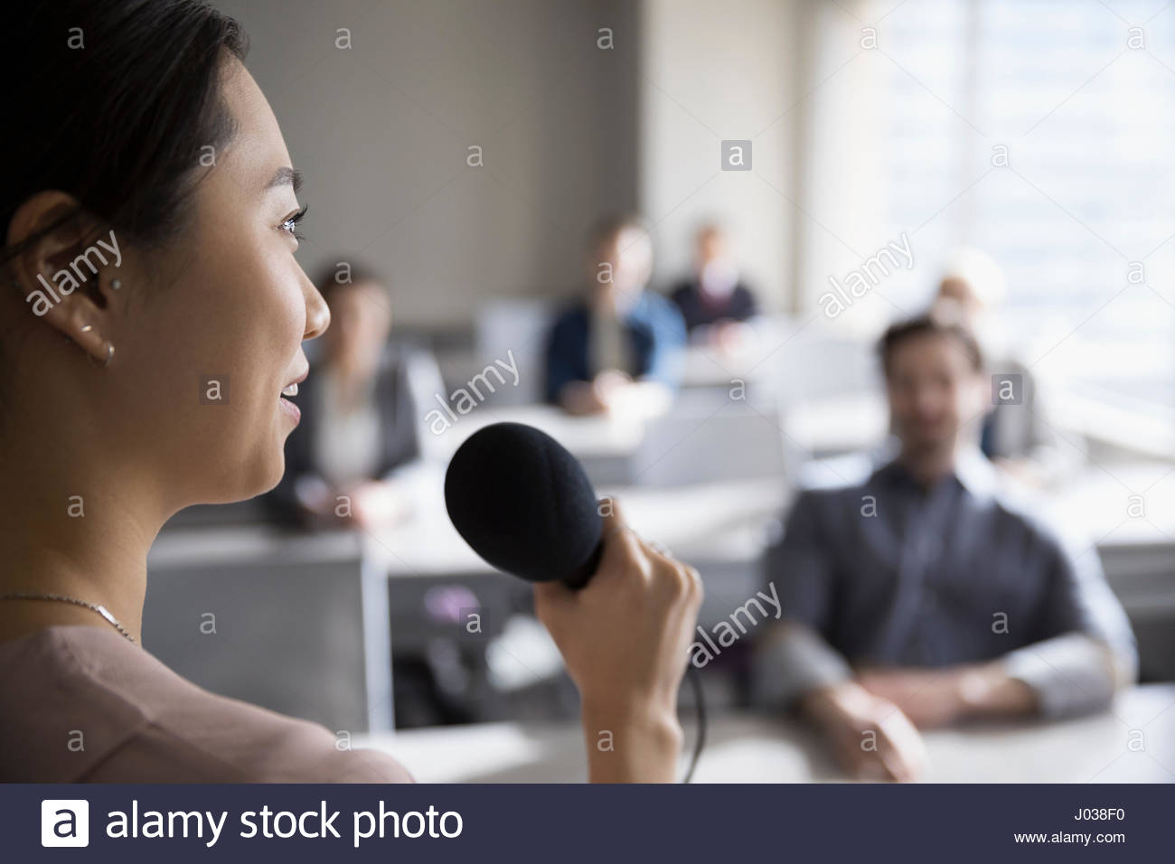 Businesswoman with microphone speaking to business people in classroom Stock Photo