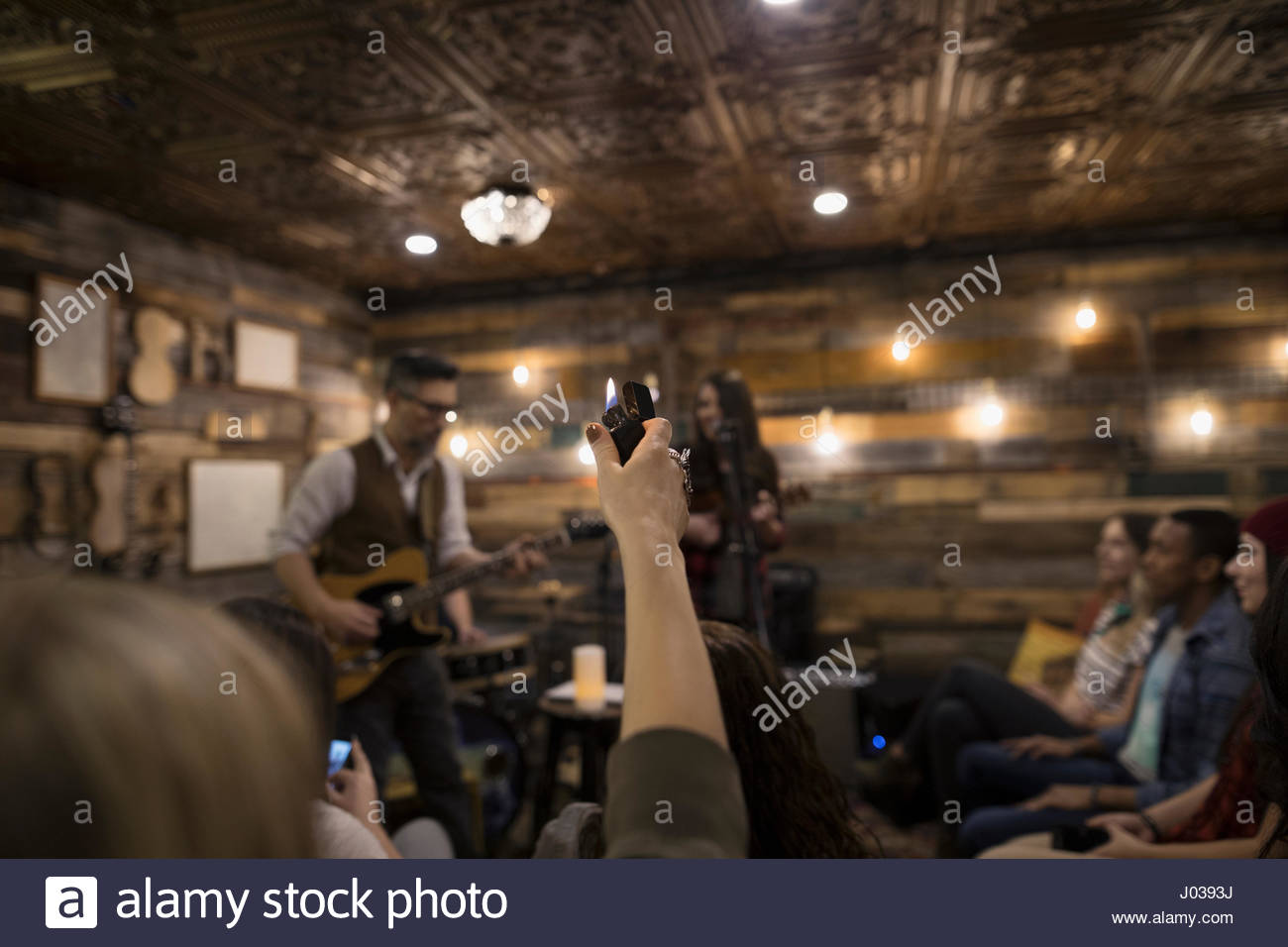 Young woman holding lighter in audience, listening to musicians on