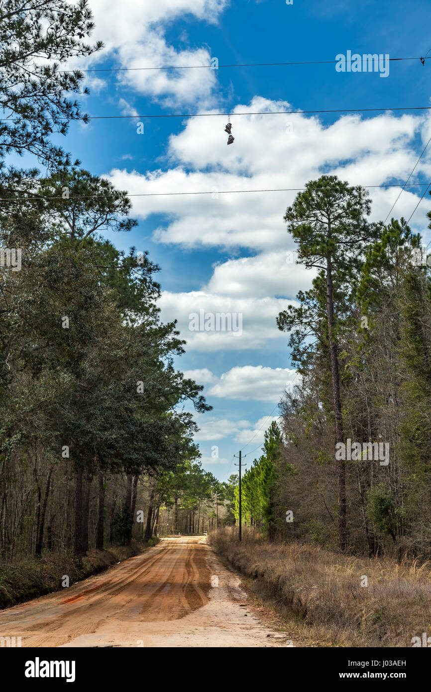 A pair of shoes hang from a power line above a dirt road in Southeastern Georgia. Stock Photo