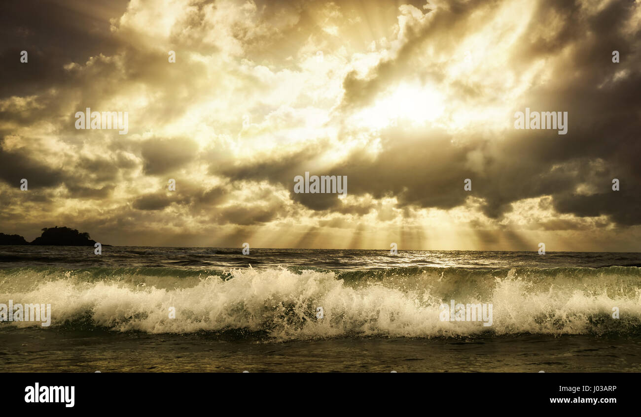 Dramatic cloudscape over the sea with rays of sunlight and a foaming wave in the foreground, toned warm colors Stock Photo