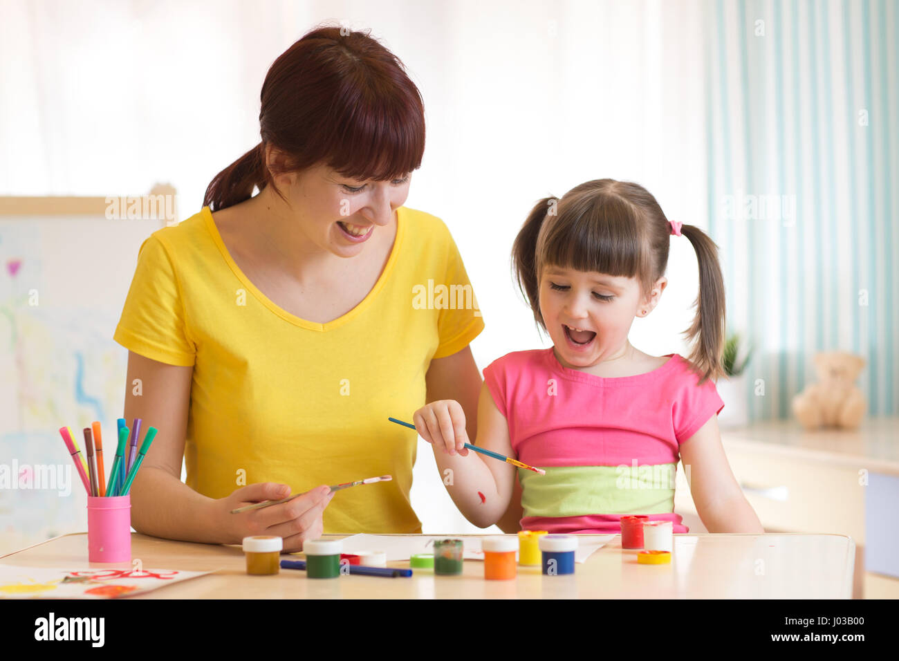 Happy kid and mom together paint. Adult woman helps the child girl. Stock Photo
