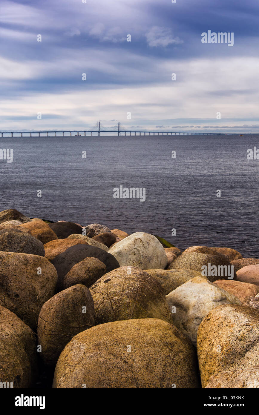 Large rocks on the sea shore, seascape and Oresund bridge in the background on cold winter day with dramatic sky Stock Photo