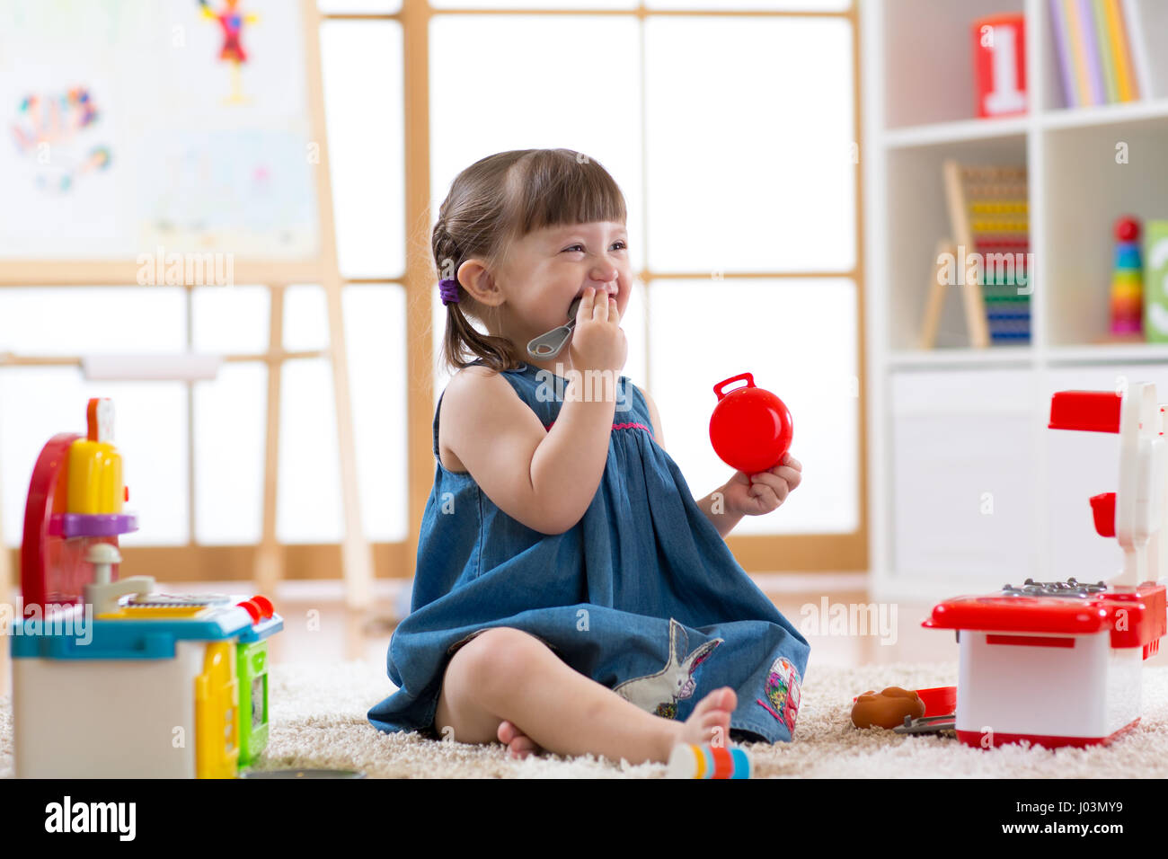 Pretty child girl playing with a toy kitchen in children room Stock Photo