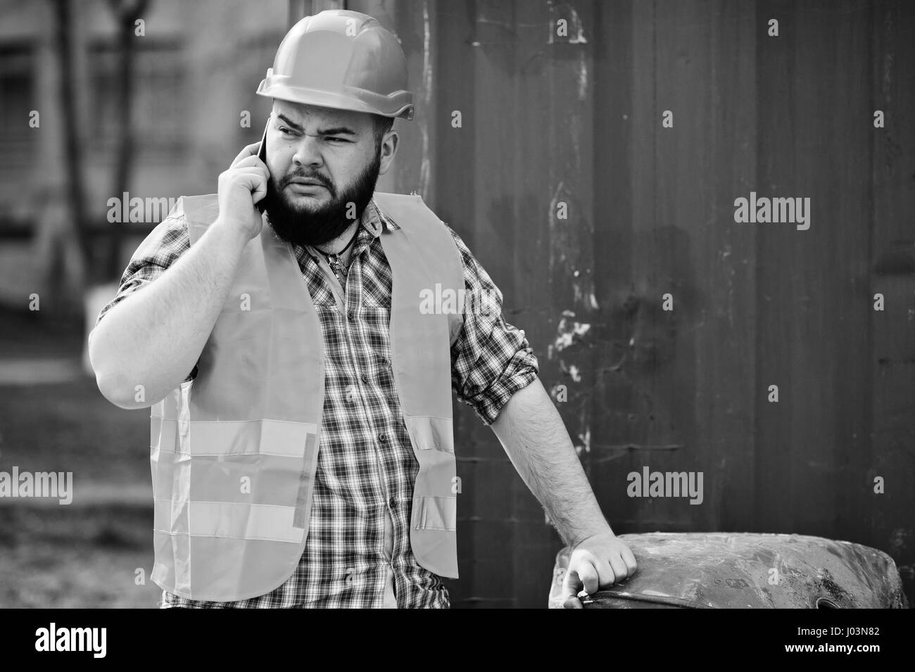 Brutal beard worker man suit construction worker in safety orange helmet near red barrel speak on phone. Stock Photo