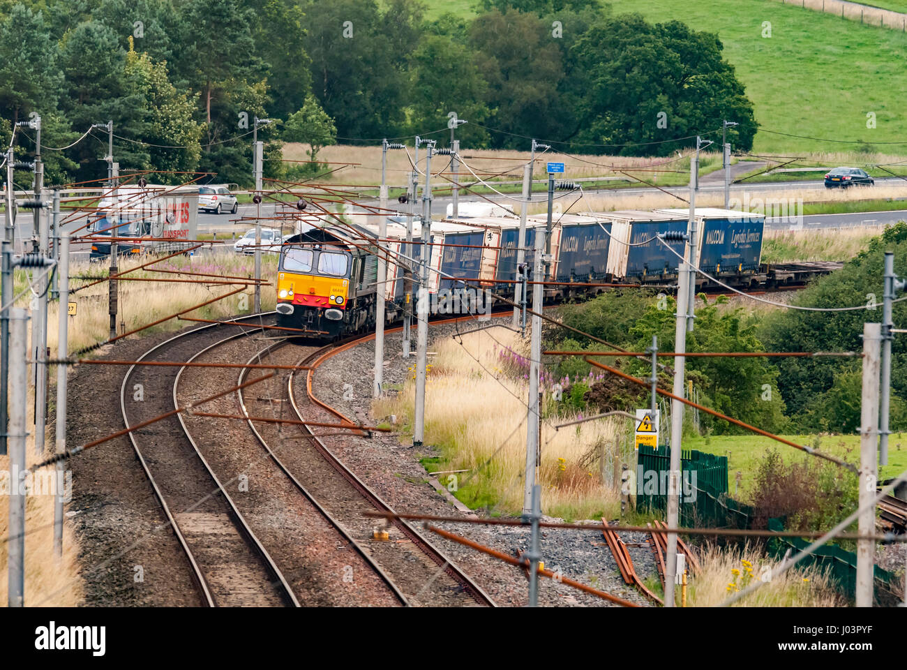 Class 66 locomotive hauling freightliner wagons on the West Coast Main Line in Cumbria passing the M6 motorway. Stock Photo