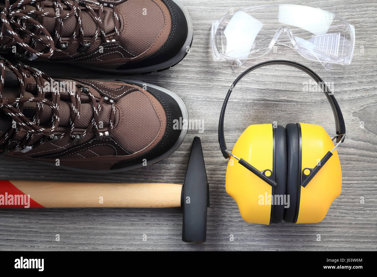 Working tools and clothes on wooden background. Close-up of protective glasses and headphone from above. Hammer with wood handle. New working shoes cl Stock Photo