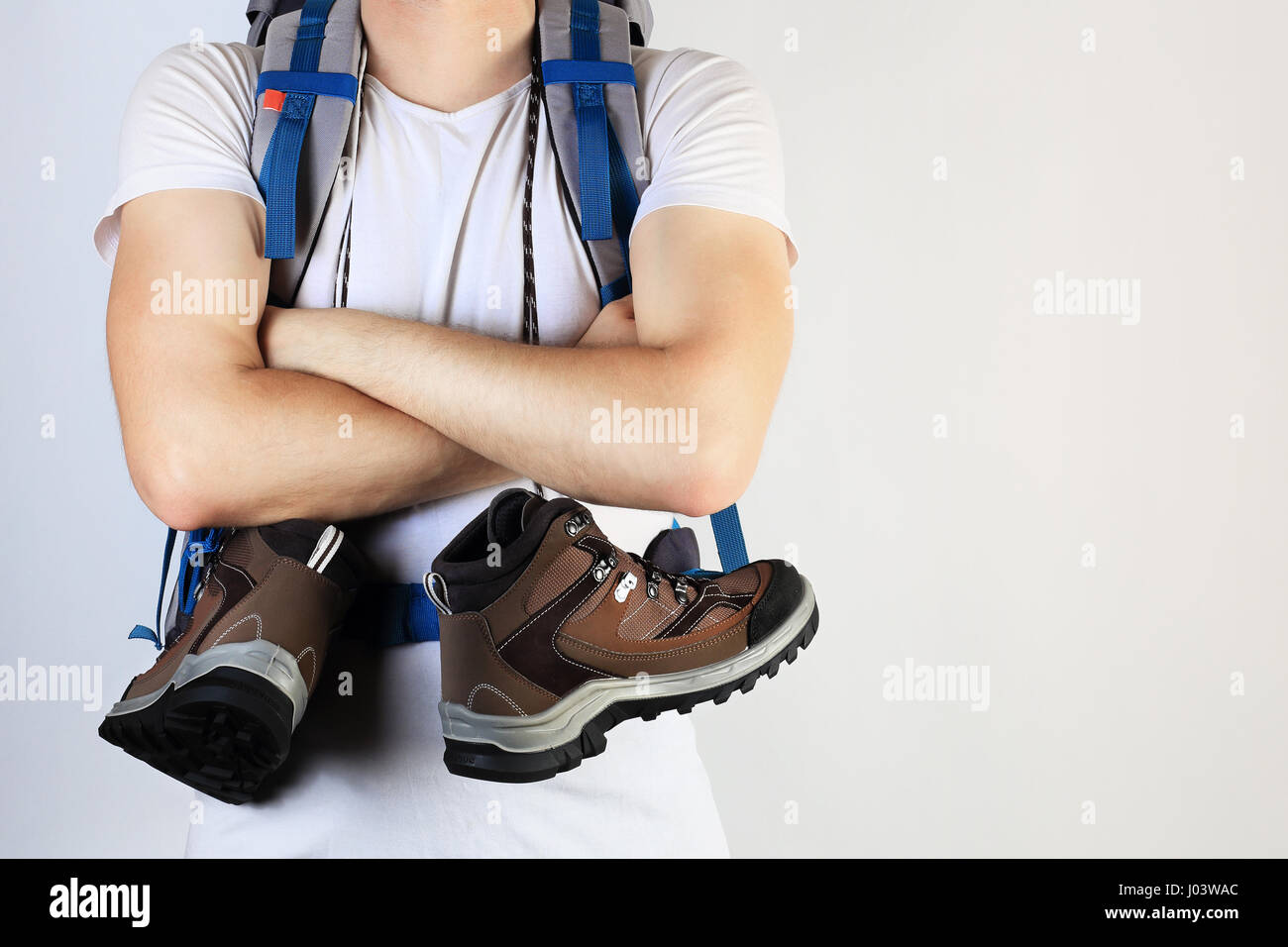 Trekking shoes on hiker neck. Traveler with new shoes and blue backpack on white background. Bright travel and hiker background. Stock Photo