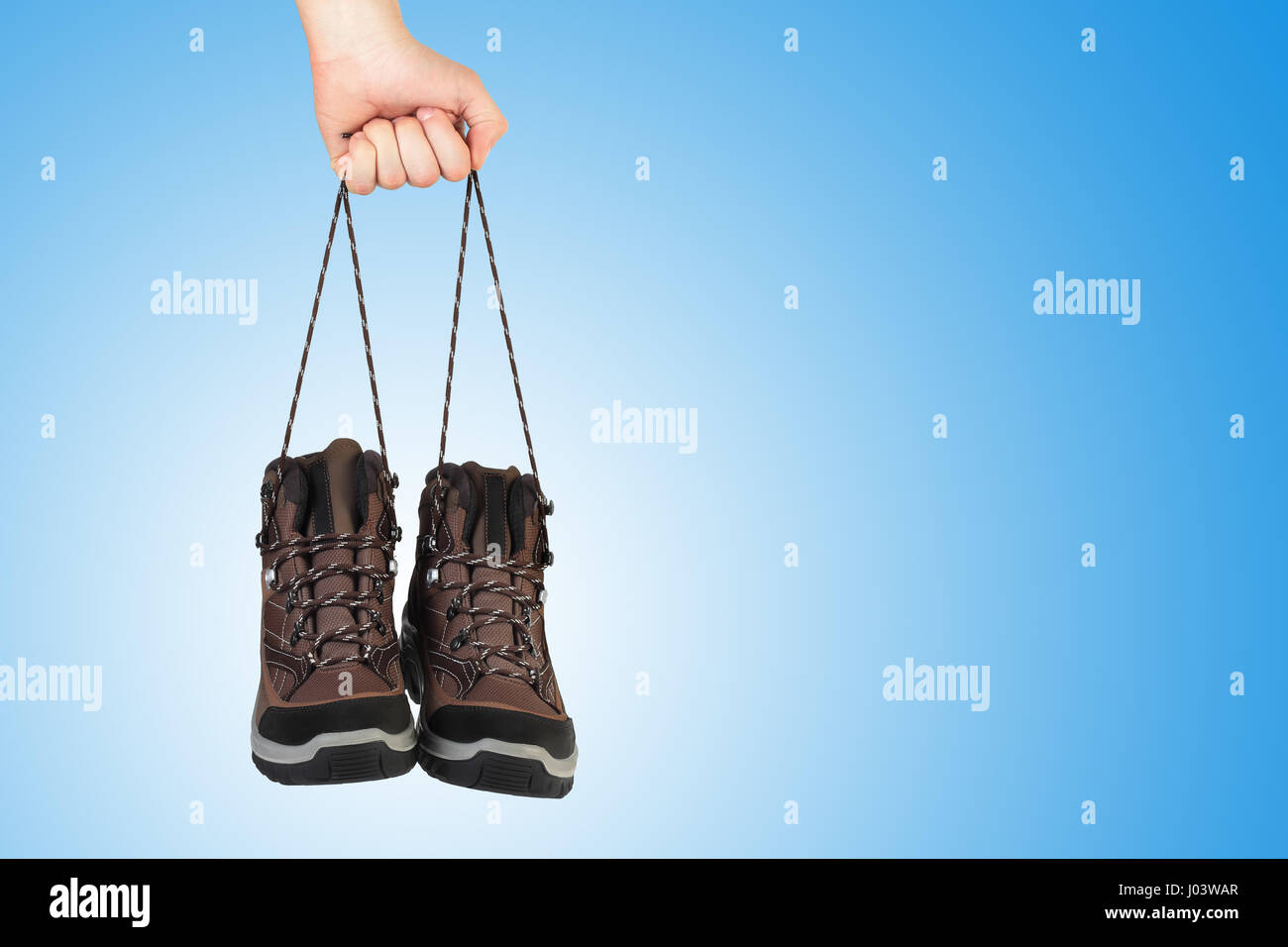 New shoes in hand on blue background. Hand hold shoes by shoelaces. Sale background with copyspace on blue background. Stock Photo
