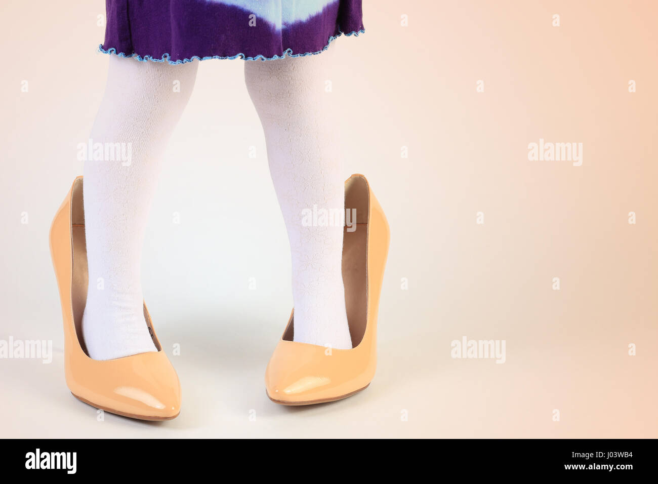 Child trying on high heel shoes. Close-up of child feet in yellow shoes. Little girl play with mother's shoes. Funny child background. Stock Photo