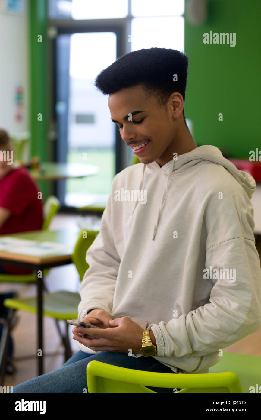 Teenage student using his smartphone during lesson. He is looking at the screen and smiling. Stock Photo