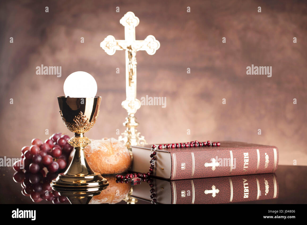 Catholic religion theme.  Holy Bible, the cross and gold chalice on glass table and stone background. Stock Photo