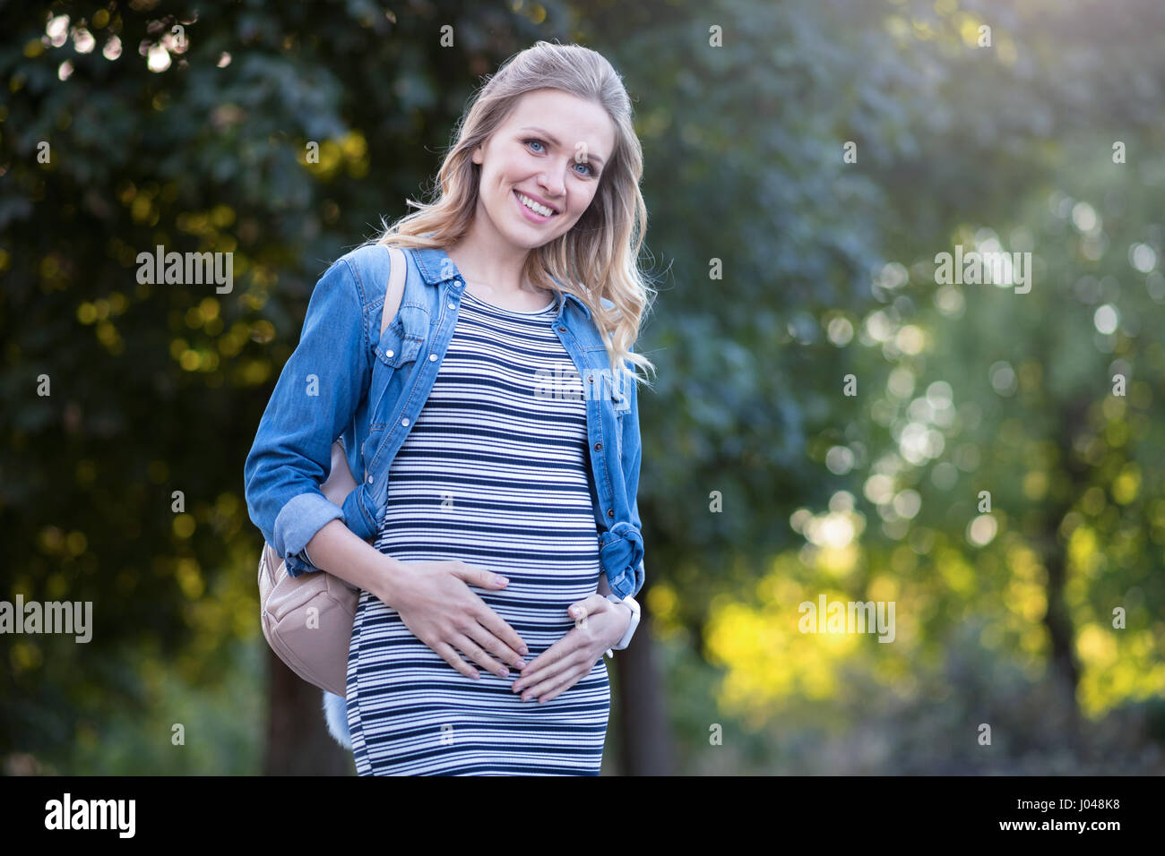 Peaceful young pregnant woman touching her belly outdoors Stock Photo