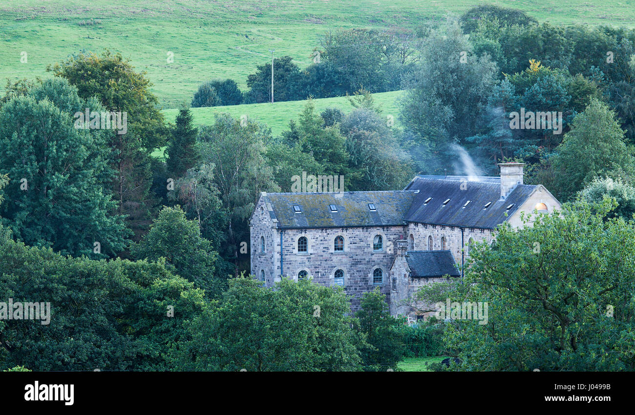 A view of a farmhouse in Longnor, North Staffs set in a belt of trees. on a late summer evening. The farmhouse shows a small curl of smoke from a chim Stock Photo