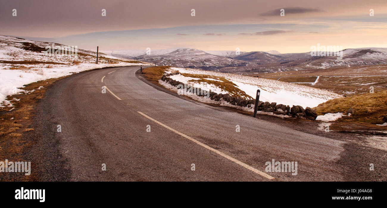 The 2-lane Buttertubs Pass road winds across snow-covered moors, looking down towards Hawes and Wensleydale in England's Yorkshire Dales in winter. Stock Photo