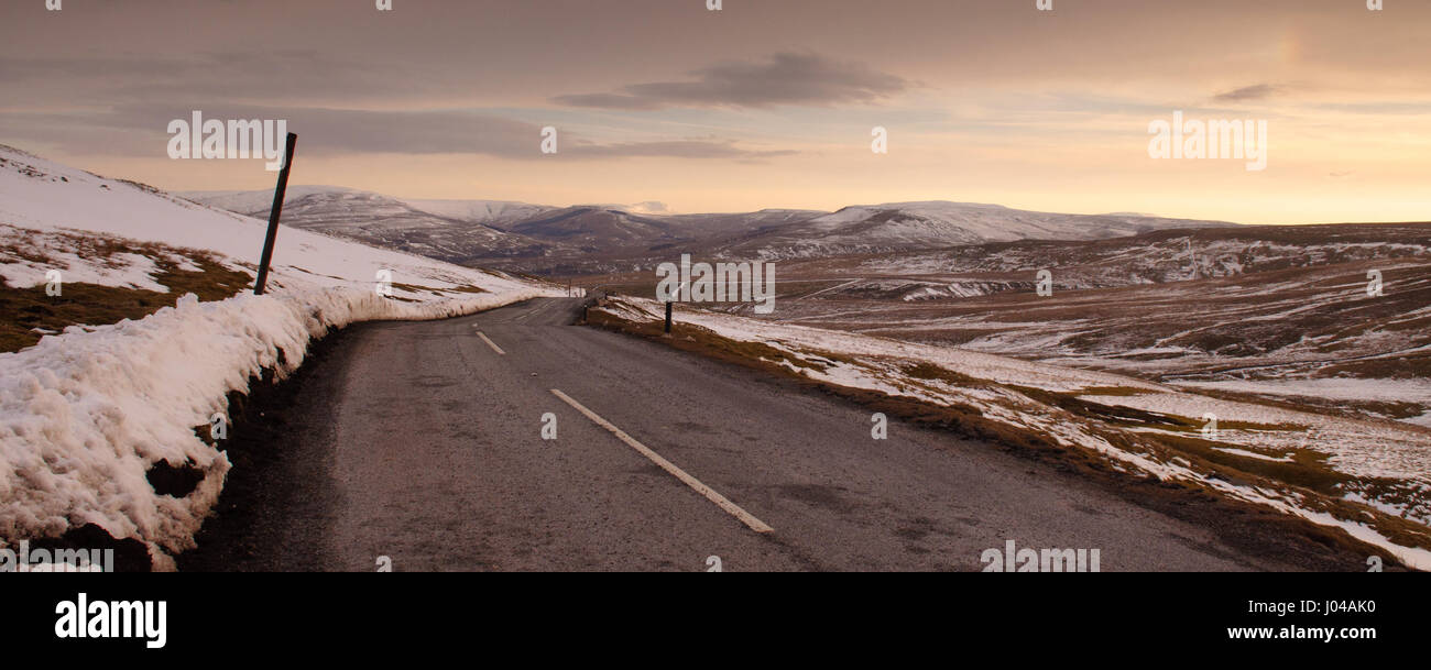 The 2-lane Buttertubs Pass road winds across snow-covered moors, looking down towards Hawes and Wensleydale in England's Yorkshire Dales in winter. Stock Photo