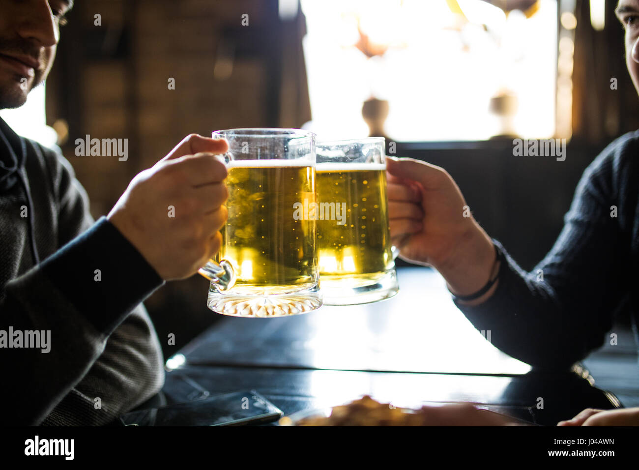 people, leisure and drinks concept - close up of male hands clinking beer glasses and pretzels at bar or pub Stock Photo