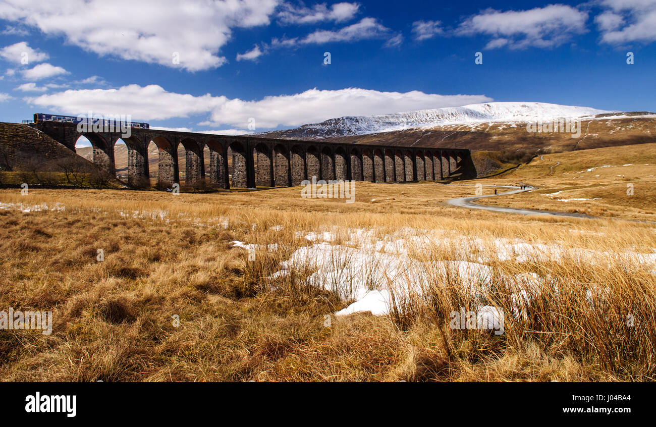 Ribblehead, England, UK - April 1, 2013: A Northern Rail Class 158 diesel passenger train passes the snow-covered mountain of Whernside as it crosses  Stock Photo