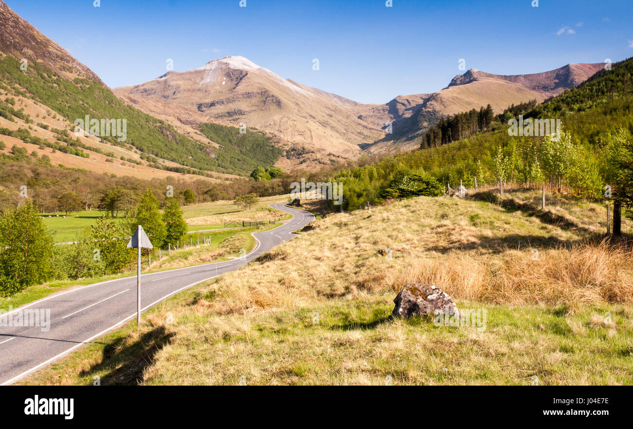 A small country road winds through pastures and woodland in the valley floor of Glen Nevis under the mountains of Ben Nevis in the West Highlands of S Stock Photo