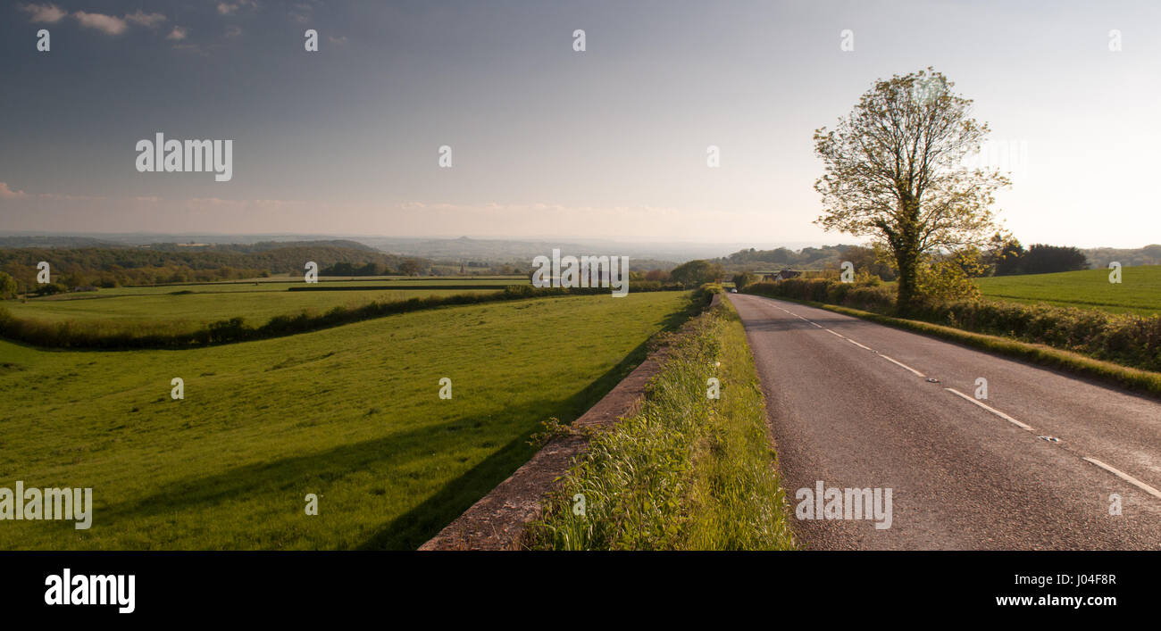 A road runs through agricultural fields and pastures across the Mendip Hills towards the Somerset Levels in south west England. Stock Photo