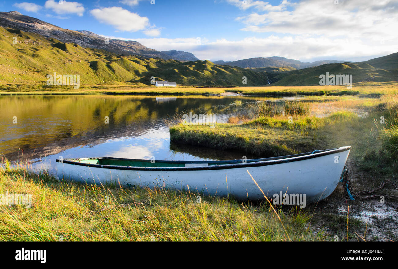 A traditional woden rowing boat rests on the banks of a small lake, or lochan, in the valley of Glen Torridon, beneath the Torridon Hills mountains in Stock Photo