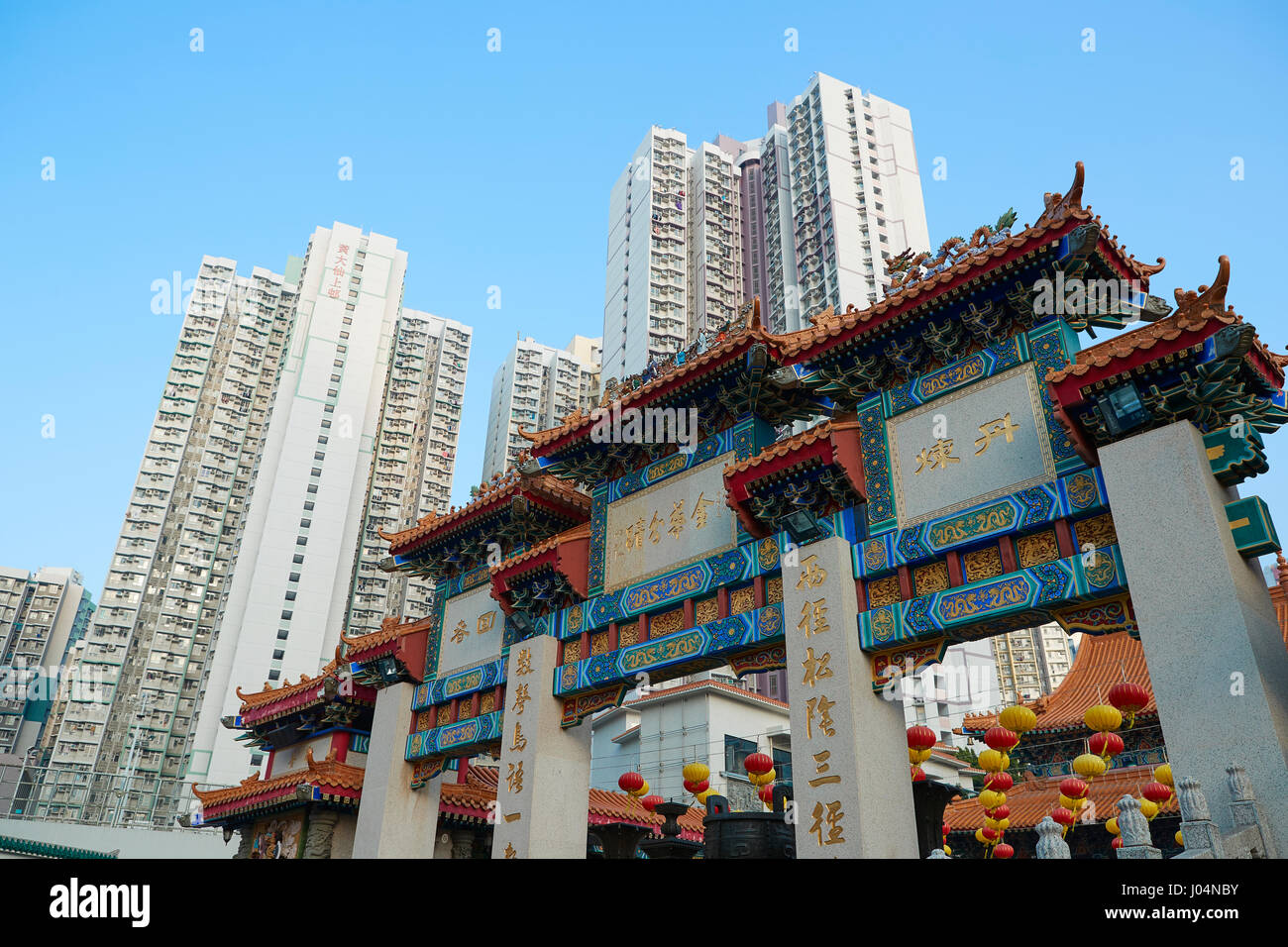 Ornate Traditional Chinese Gateway Contrasts With The Kowloon Skyline At The Wong Tai Sin Temple, Hong Kong. Stock Photo
