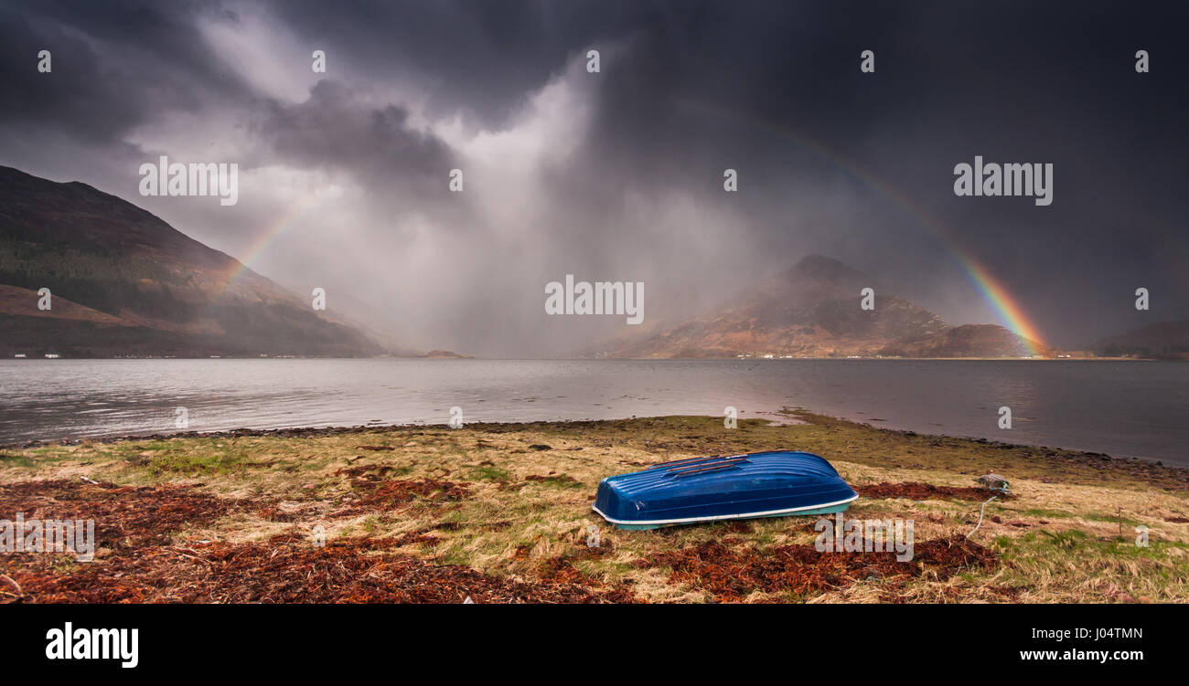 A partial rainbow stands at the foot of Glen Shiel as a storm passes over Loch Duich and the Five Sisters of Kintail mountains. Shot from Ratagan acro Stock Photo