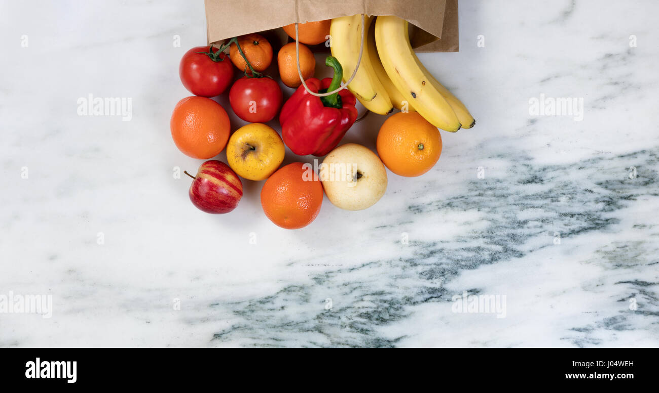 Flat lay view of fruits and vegetables spilling out of a paper bag onto ...