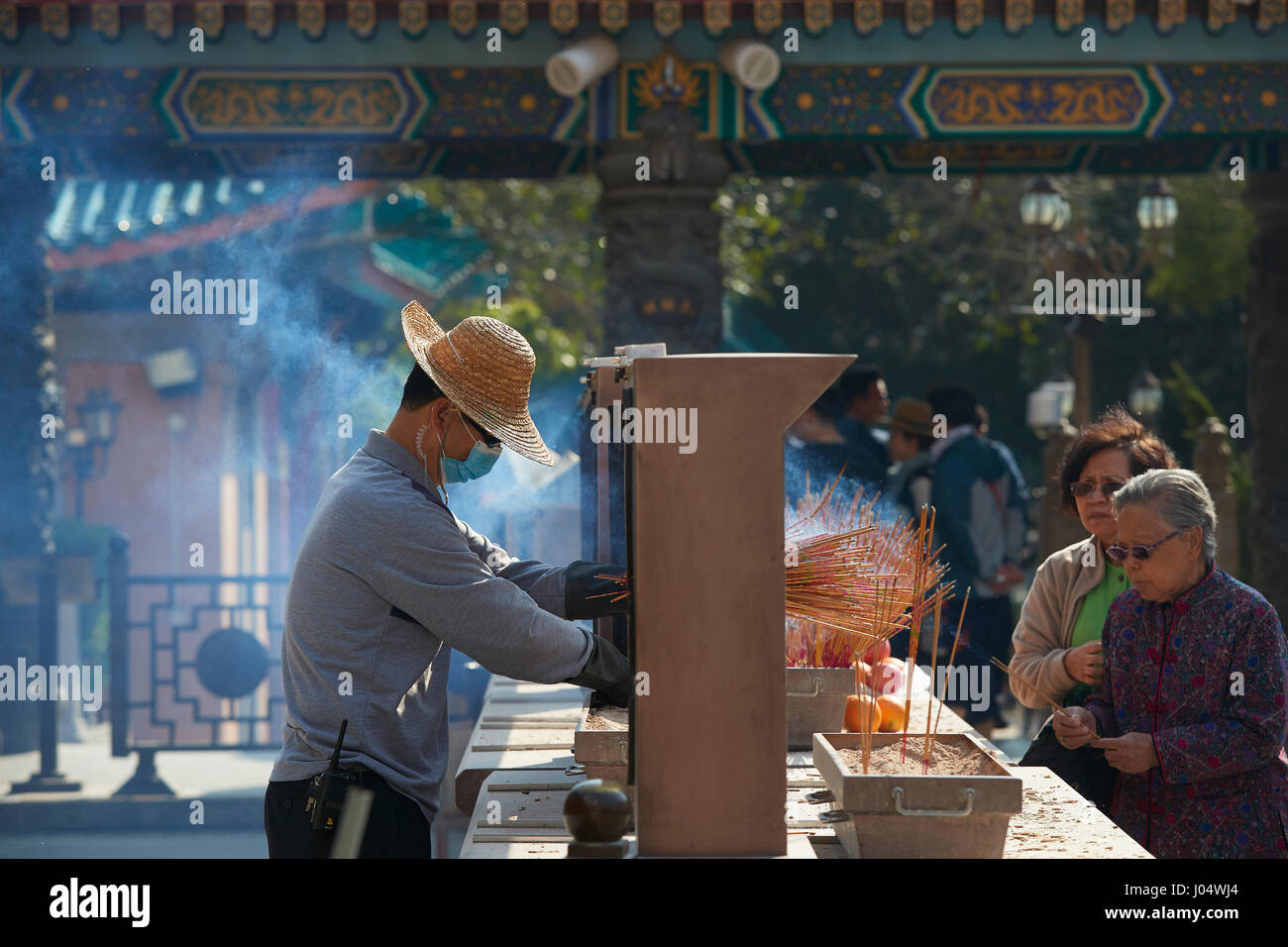 Man Tidies Burning Incense At The Wong Tai Sin Temple, Hong Kong. Stock Photo