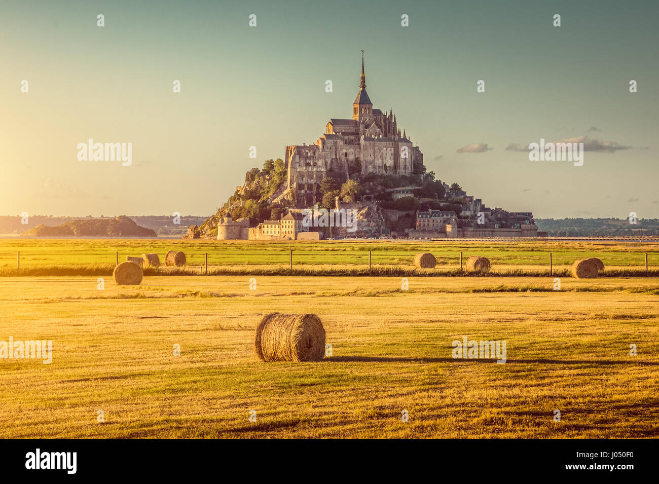 Beautiful view of famous historic Le Mont Saint-Michel in golden evening light at sunset in summer with hay bales on fields, Normandy, France Stock Photo